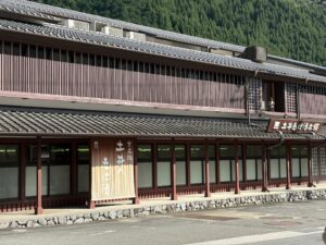 「京名物 土井の志ば漬」ののれんが掛かる土井志ば漬本舗の建物。背後に杉の山が迫る